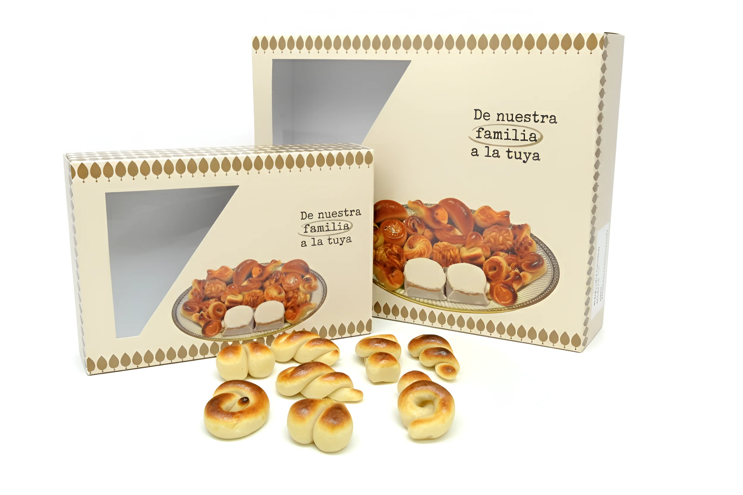 Figuras de mazapán Dos cajas de cartón beige con un patrón de rombos marrones y la frase "De nuestra familia a la tuya". Ambas cajas tienen una ventana transparente que muestra un surtido de dulces de mazapán y almendra. En primer plano, varios dulces de mazapán en espiral y con forma de lazo están esparcidos.