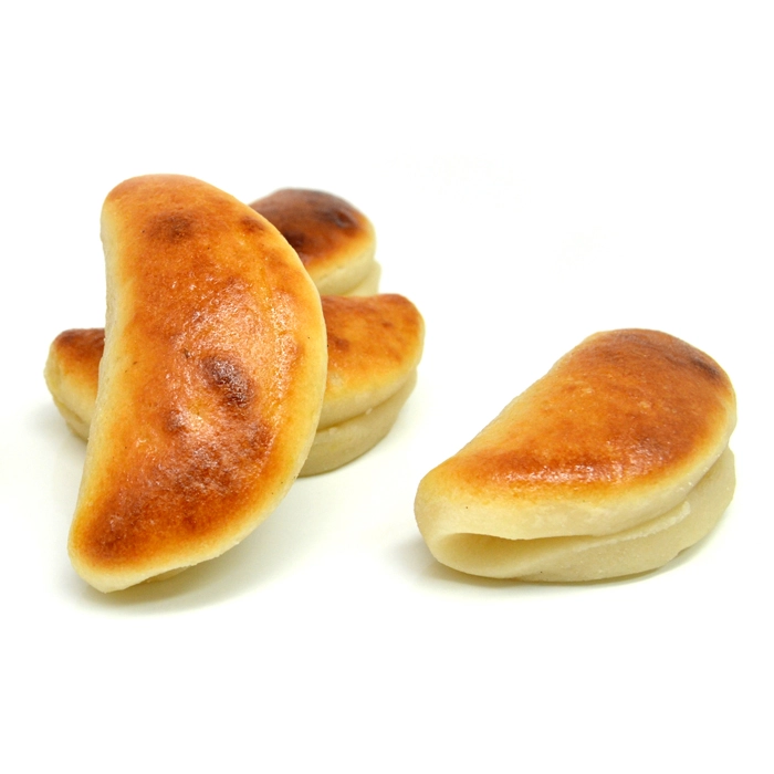 Varias piezas de mazapán con forma de media luna, con un acabado ligeramente tostado en la parte superior, dispuestas sobre un fondo blanco. Dos están apiladas al fondo y una está de lado en primer plano.