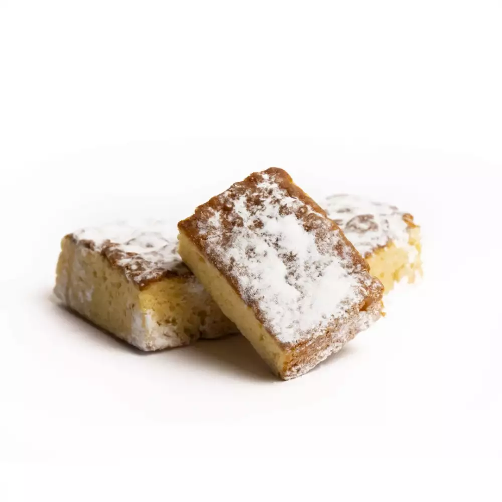 Tres trozos rectangulares de bizcocho o mazapán, espolvoreados con azúcar glas, apilados informalmente sobre un fondo blanco.